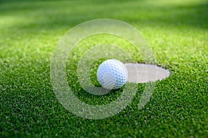 Closeup of white golf ball next to the cup on a putting green