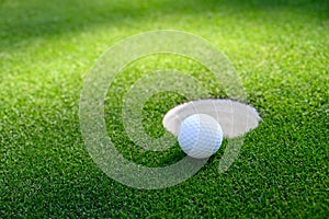 Closeup of white golf ball next to the cup on a putting green