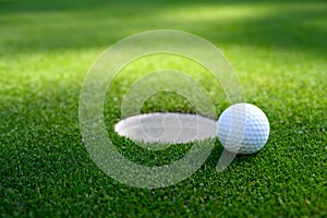 Closeup of white golf ball next to the cup on a putting green