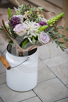 Closeup of white metal bucket full of beautiful flowers. Flowers in vase on concrete background. Summer or spring. Outdoor