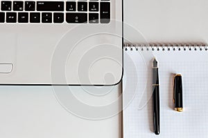 Closeup of white office desk with laptop, note book and  fountain pen. Top view with copy space