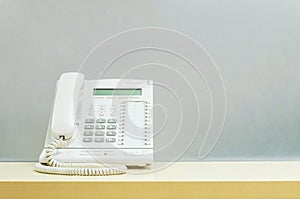 Closeup white phone , office phone on blurred wooden desk and frosted glass wall textured background in the work office