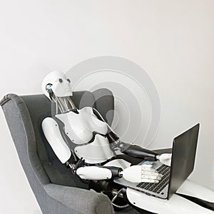 Closeup of white plastic robot working with laptop while sitting in armchair