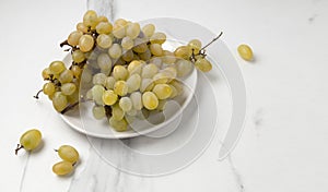 Closeup of white plate full of delicious sweet grape on the marble kitchen table.Empty space
