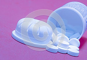 Closeup of white round pills pouring out of the medicine bottle on pink background