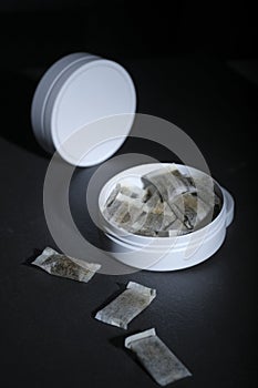 Closeup of a white swedish snus can and portion snuff pouches against a dark background