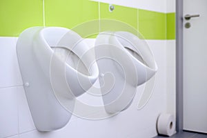 Closeup of white urinals in men`s bathroom, design of white ceramic urinals for men in toilet room.