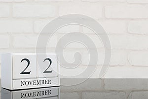 Closeup white wooden calendar with black 22 november word on black glass table and white brick wall textured background with copy