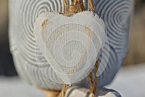 closeup on white wooden heart held by strings in front of decorative flowerpot