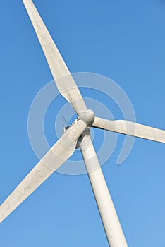 Closeup of a wind turbine and propellor blades against a blue sky background from below. Harvesting a sustainable and