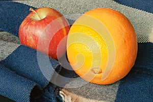 Closeup of winter fruit, an orange and apple, resting on a winter scarf with blue and white stripes or plaid.