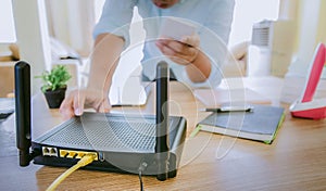 Closeup of a wireless router and a man using smartphone on living room at home ofiice, equipment for  working from home, while in