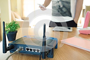 Closeup of a wireless router and a young man using a smartphone on living room at home with a window in the background