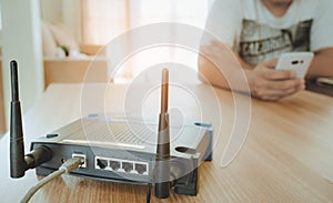 Closeup of a wireless router and a young man using a smartphone on living room at home with a window in the background