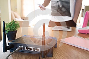 Closeup of a wireless router and a young man using a smartphone on living room at home with a window in the background .