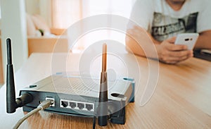 Closeup of a wireless router and a young man using a smartphone on living room at home with a window in the background . photo