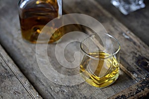 Closeup of a wisky glass and bottle on a rustic shabby wooden table from a high angle