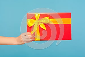 Closeup of woman arm holding red gift box with yellow ribbon, romantic surprise for Valentine`s day