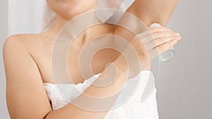 Closeup of woman covered in white bath towel lifting her arm up and using deodorant. Concept of hygiene, natural beauty, feminity