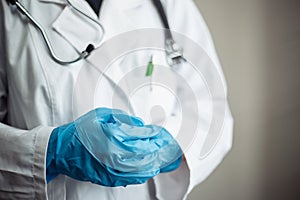 Closeup of a woman doctor wearing white medical gown and blue gloves, stethoscope. Female nurse holding her hands together crossed photo