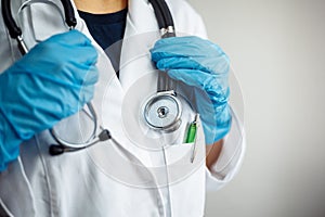 Closeup of a woman doctor wearing white medical gown and blue gloves, stethoscope. Female nurse holding a stethoscope on her neck
