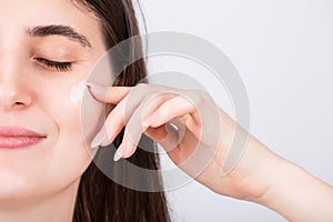 Closeup woman face applying moisturizing cream, isolated on white background. Skin care concept