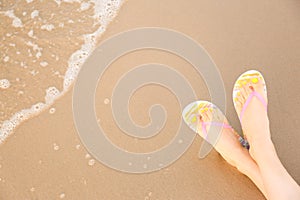 Closeup of woman with  flip flops on sand near sea, space for text. Beach accessories
