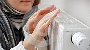 Closeup of woman freezing at home warming hands at heating radiator. Concept of energy crisis, high bills, broken heating system,