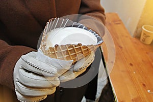 Closeup of woman girl hands in white gloves holding a cornettoccino, coffee with ice cream and milk in a waffle cone with