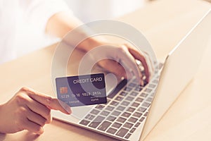 Closeup woman hand holding credit card on hand and typing code on laptop