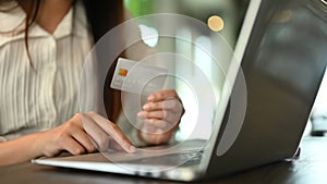 Closeup woman hand holding credit card and typing on laptop, making online shopping or paying bills