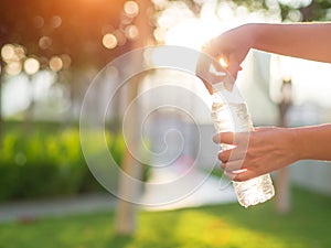 Closeup woman hand holding drinking water bottle during sunset.