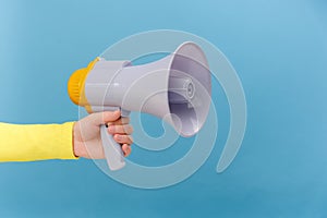 Closeup of woman hand holding megaphone, announcing of advertisement or protesting, posing isolated over plain blue color