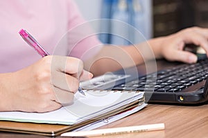 Closeup a woman hand holding pen and using a laptop computer working at her desk in the office. A businesswoman is writing down he