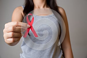 Closeup woman hand holding red ribbon HIV, world AIDS day awareness ribbon. Healthcare and medicine concept