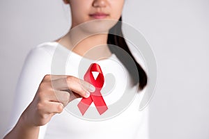 Closeup woman hand holding red ribbon HIV, world AIDS day awareness ribbon. Healthcare and medicine concept