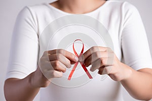 Closeup woman hand holding red ribbon HIV, world AIDS day awareness ribbon. Healthcare and medicine concept