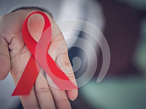 Closeup woman hand holding red ribbon HIV