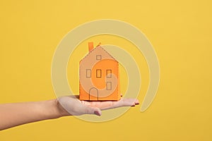 Closeup of woman hand holding small orange paper house, concept of dream home purchase, mortgage.