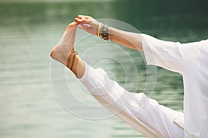 Closeup of woman hand and leg practice yoga by the lake