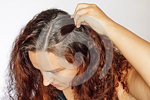 Closeup of woman hand pushing back strand of hair to show graying hair roots on white background. Regrown roots which