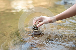 Closeup woman hand to doing Stone stacked in water river stream