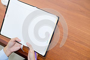 Closeup woman hand writing on notebook on wooden table, girl work with paper at coffee shop