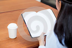 Closeup woman hand writing on notebook on wooden table, girl work with paper at coffee shop