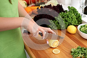 Closeup of woman hands cooking vegetables salad in kitchen. Housewife cuts lemon. Healthy meal and vegetarian concept.