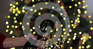 Closeup of woman hands opening bottle of champagne on background of Christmas . Woman hands open bottle of sparkling