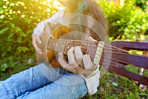Closeup of woman hands playing acoustic guitar on park or garden background. Teen girl learning to play song and writing music