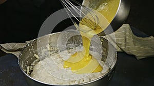 Closeup woman hands pour whisked egg yolks into metal bowl with yeast dough