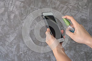 Closeup woman hands using spray alcohol sanitizer cleaning screen smartphone, to prevent the virus and bacterias. Clean smartphone