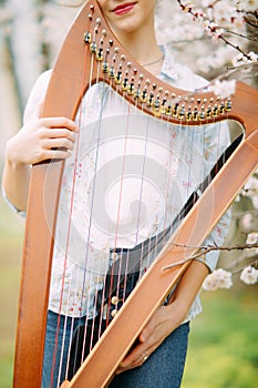 Closeup woman harpist with harp among flowering garden